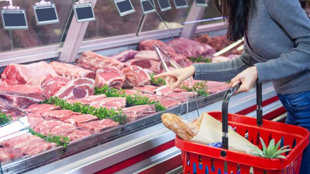 A shopper looking at display of meat at the butcher's counter in a supermarket
